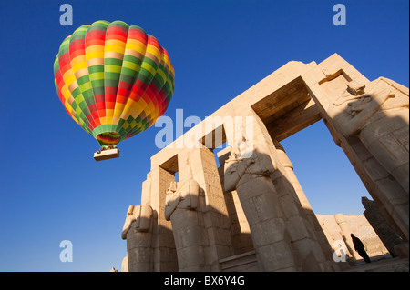 Ein schönen und bunten Heißluftballon schwebt sanft über die Statuen und die Ruinen eines antiken ägyptischen Tempels bei Sonnenaufgang Stockfoto