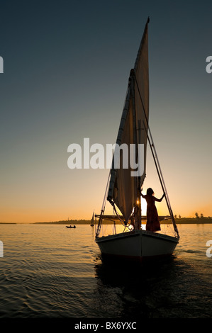 Eine beeindruckende und schöne Bild von einem traditionellen ägyptischen Segelboot bezeichnet eine Feluke auf dem Nil bei Sonnenuntergang mit Mädchen an Bord Stockfoto