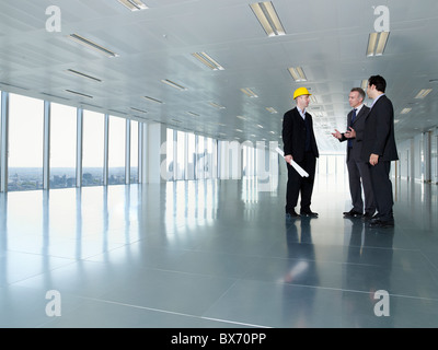 Drei Führungskräfte, in Bauarbeiterhelm, in leeren Büroflächen Stockfoto