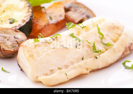 Tilapiini-Filet mit Champignons, Zucchini und Karotten als Closeup auf einem weißen Teller Stockfoto