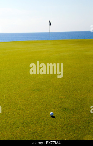 Golfball auf Putting Green mit Fahnenstange und dem Pazifischen Ozean im Puerto Los Cabos Golf Club in San Jose del Cabo, Mexiko Stockfoto