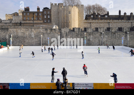 Menschen, die eine temporäre Eislaufbahn nutzen, die in einem Trockengraben vor dem Hintergrund des historischen Tower of London für die Weihnachtszeit in England errichtet wurde Stockfoto