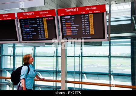 Frau stehend und CRT-Monitore für Abflug-und Ankunftszeiten am neuen modernen Flughafen in Südostasien in Singapur anzeigen Stockfoto