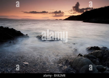 Wellen, die auf einem felsigen Kiesstrand bei Sonnenuntergang während einer Langzeitbelichtung erstellen schöne und mystische Bilder von Schottland Stockfoto