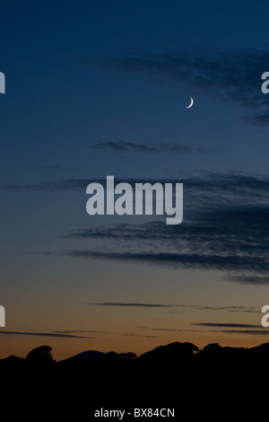 Ein Halbmond scheint hinter Luftschlangen Wolke über der Lleyn-Halbinsel bei Sonnenuntergang. Stockfoto