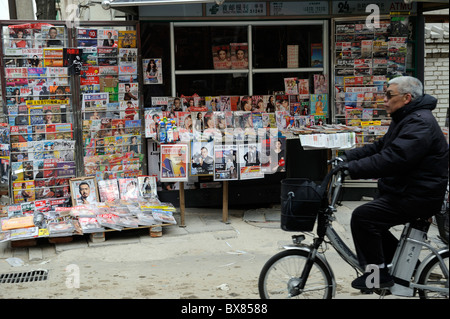 Ein älterer Mann fährt Fahrrad vorbei an einem Kiosk in Peking, China.12-Dec-2010 Stockfoto