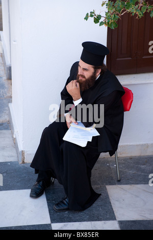 Orthodoxe Papst seinen Bart beim Sitzen im Hof der Panagia Evangelistria in Tinos Stadt entwirren. Stockfoto