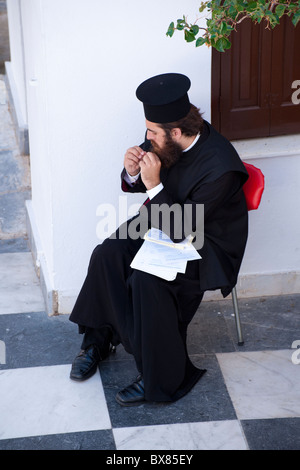 Orthodoxe Papst seinen Bart beim Sitzen im Hof der Panagia Evangelistria in Tinos Stadt entwirren. Stockfoto