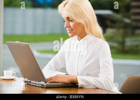 Junge erfolgreiche lächelnde Frau schaut auf ihrem laptop Stockfoto