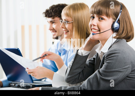 Porträt von lächelnden Geschäftsfrau Blick in die Kamera mit Telefon und sitzen am Tisch auf dem Hintergrund zwei Geschäftsleute Stockfoto