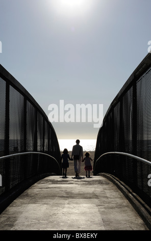 Eine Mutter und zwei Töchter überqueren eine Brücke, wie sie nähern sich den Ozean in Santa Monica, Los Angeles, Kalifornien. Stockfoto