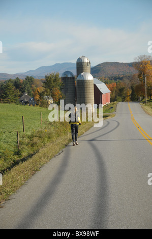 Eine Frau läuft entlang einer Landstraße mit einer Farm im Hintergrund in Waitsfield, Vermont Stockfoto