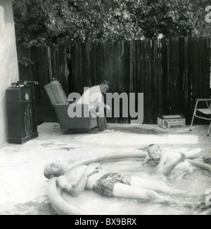 Vater und Sohn Entspannung in Schwimmbad Mann sitzt Sessel tube Radio Amerika der 1950er Jahre tragbare Hinterhoflache heißen Tag Sommer Stockfoto