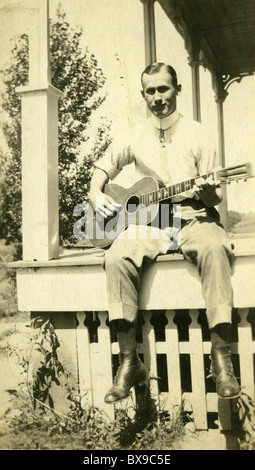 Mann sitzt auf Holz Veranda, Gitarre zu spielen, während die 1920s 1930s Volksmusiker Musik Americana schwarz / weiß Stockfoto