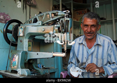 Lächelnd Schuster sitzen durch eine Nähmaschine in seinem Geschäft Quoseir Dorf, Rotes Meer, Ägypten. Stockfoto