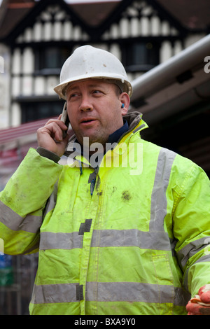 Ein Mann gekleidet in 'hi-viz' Jacke und Schutzhelm, macht einen Anruf auf seinem Handy. Stockfoto