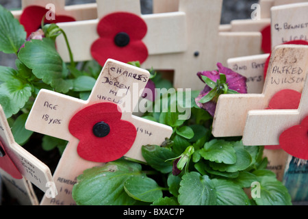 Nahaufnahme der Miniatur aus Holz kreuzt mit Mohnblumen, die neben einem Kriegerdenkmal befestigt. Stockfoto