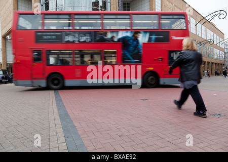 Eine Frau kreuzen die Straße als Doppeldeckerbus vorbei, Kingston, Surrey, England. Stockfoto