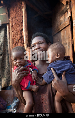 Eine Frau (Frau Regina Nabirye) hält ihr Säugling Zwillingen vor ihrem Haus in einem Slum in Jinja, Uganda, Ostafrika. Stockfoto