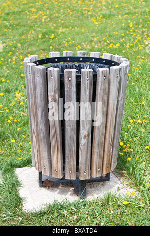 Ein hölzerne Mülleimer sitzt auf dem Löwenzahn gefüllten Rasen in einem lokalen Park. Stockfoto