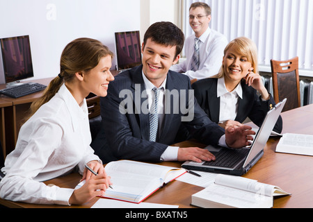 Porträt von drei jungen Leuten am Tisch sitzen mit geöffneten dicke Bücher und Laptop drauf und einen sitzenden Mann im Hintergrund Stockfoto