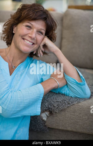 Frau, stützte sich auf Sofa und lächelnd Stockfoto