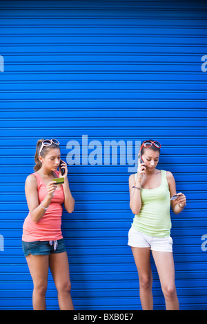 Zwei Girls vor der blauen Wand am Telefon sprechen Stockfoto