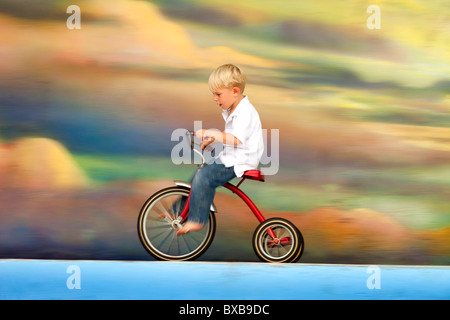 Kleiner Junge Reiten Dreirad gegen bunte Himmel mit Wolken Stockfoto