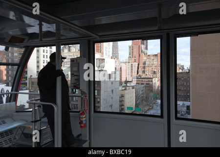 Ein Kabine Betreiber übernimmt die Roosevelt Island Tram aus der Manhattan-Station, mit Nebengebäuden Ost im Blick in New York City Stockfoto