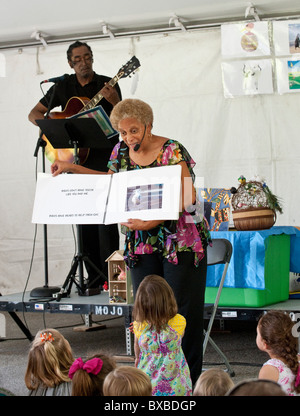 Jugendliche sehen und hören Sie Kinderbuchautorin aus Buch zu lesen, während Gitarrist hinter ihr auf dem Texas Book Festival spielt Stockfoto