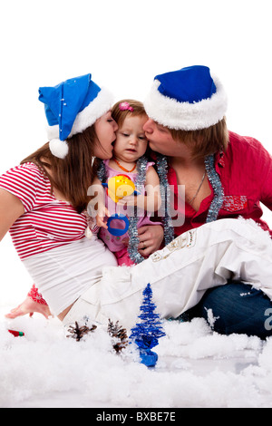 Eltern in Nikolausmütze küssen ihres Kindes in Kunstschnee isoliert auf weiss Stockfoto