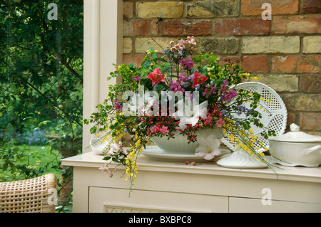 Stillleben mit weißen Lilien und gelben Ginster im Frühsommer informellen Blumenarrangement in der Schale am Tisch Stockfoto