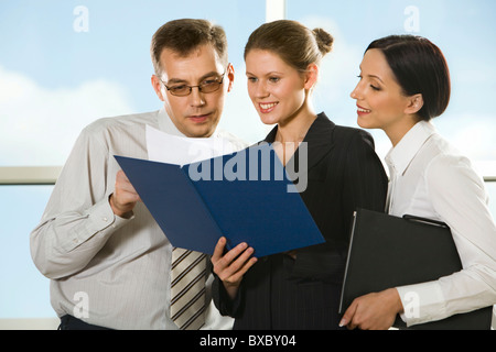 Lächelnde junge Frau zeigt Dokumente zu ihrem Chef und neugierige Mädchen auf der Suche in der Hülle Stockfoto