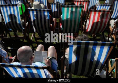 Menschen Sie sitzen entspannen in der Sonne lesen in bunten Liegestühlen in Torquay promenade Stockfoto