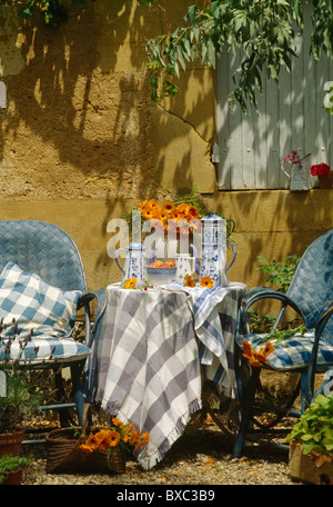 Grau + weiß aufgegebenes Tuch auf dem Tisch mit Kaffeekannen vor alten Steinmauer im Garten im Sommer Stockfoto