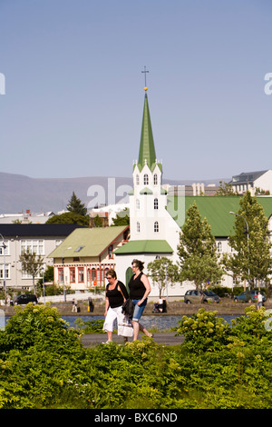 Zwei Frauen gehen Tjörnin See, Frikirkjan Kirche im Hintergrund. Reykjavik Island Stockfoto