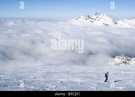 Eine Skifahrerin auf dem Gletscher von La Meije in La Grave, Frankreich, Skifahren über einige dicke Wolken. Stockfoto