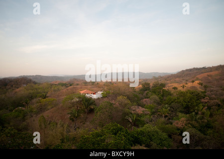 Sonne Ausbleichen über ein weißes Haus mit orange Dach in den Hügeln über den Baumwipfeln von Costa Rica Stockfoto