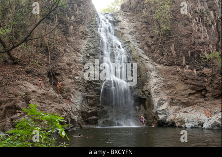 Schwimmer in einem abgeschiedenen Lagune unter einem Wasserfall Kaskadierung über eine steile Felswand Stockfoto