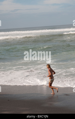 Frau im Badeanzug am Strand neben den Wellen entlang joggen Stockfoto