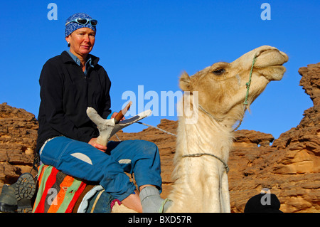 Weibliche Touristen reiten ein Mehari Dromedar in eine skeptische Stimmung bei einem Ausflug in die Acacous Berge, Wüste Sahara, Libyen Stockfoto