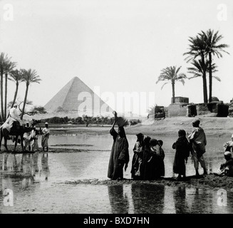 Ägypter oder Ägypter vor der Großen Pyramide von Gizeh, Teil des Gizeh Pyramidenkomplexes oder Gizeh Nekropole und Palmen, Gizeh Plateau, Groß-Kairo Ägypten. C1910 Stockfoto