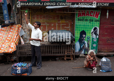 Ein Mann verkauft Spielzeug Hubschrauber während und alte Frau fleht neben ihm in Haridwar, Uttarakhand, Indien. Stockfoto