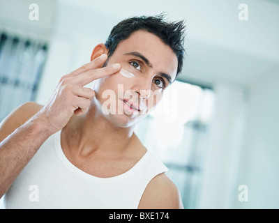kaukasischen Jüngling Augencreme auf Gesicht auftragen. Horizontale Form, Vorderansicht, Kopf und Schultern Stockfoto