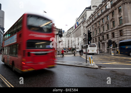 Ein London-Bus beschleunigt über eine Kreuzung vor der Royal Exchange in der City of London. Stockfoto