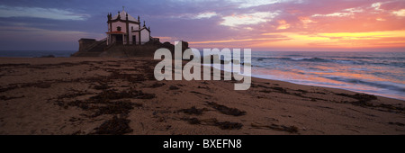 Panoramablick über Senhor da Pedra Kapelle bei Sonnenuntergang mit Algen am Strandsand Stockfoto