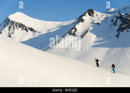 Zwei Männer Klettern auf einem schneebedeckten Berghang mit Steigfelle auf den Skiern am Col du Lautaret, in der Nähe von La Grave, Frankreich. Stockfoto