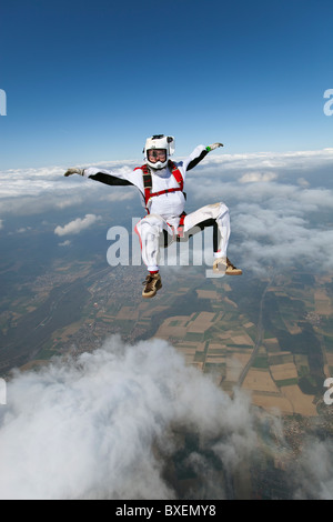 Mann mit Kamera auf seinem Helm filmt Fallschirmspringer im freien Fall über Wolken und Wiesen. Stockfoto