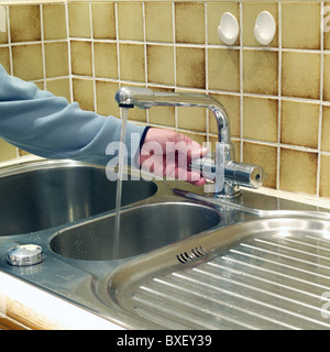 Kaukasischen Männchen Einschalten einer Mischbatterie (Wasserhahn) bei einer Küchenspüle in der häuslichen Umgebung, UK-Modell veröffentlicht Stockfoto