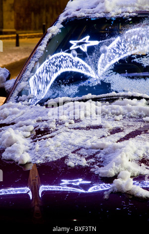 Weihnachtsbeleuchtung spiegeln sich in der Windschutzscheibe eines verschneiten Autos in Cambridge Stockfoto